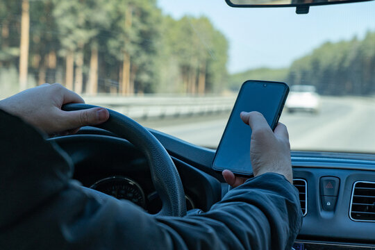A Distracted Driver Grips the Steering Wheel While Using a Smartphone on a Scenic Highway Surrounded by Trees