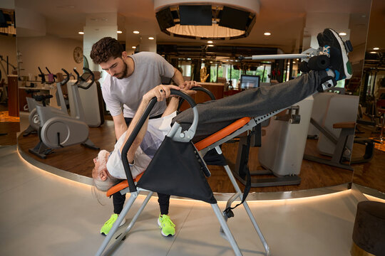 Younger man assisting older man on inversion table in gym