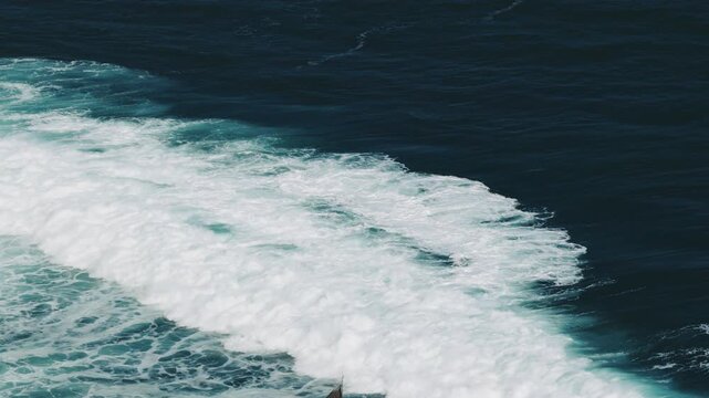 Aerial view of a powerful ocean wave breaking with white foam and sea spray on the deep blue water of Mesra Beach in Kecamatan Tanjungsari, Daerah Istimewa Yogya, Indonesia.