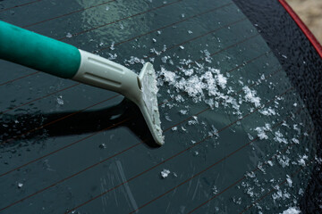Obraz premium Removing Ice and Snow from a Car Rear Window with a Scraper Tool in Cold Weather Conditions