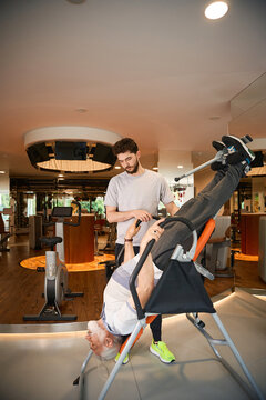 Older man using inversion table with younger male assistant indoors