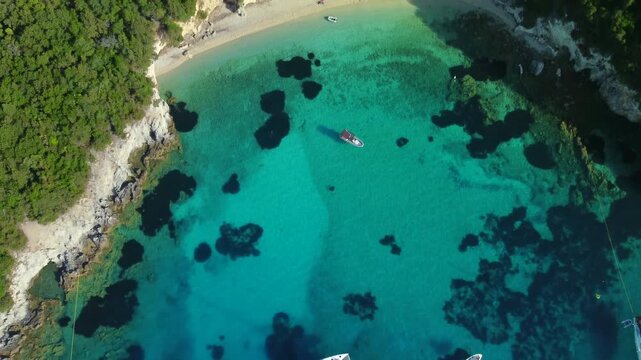 Aerial approach from luxury yachts to Blue Lagoon beach, tilting to top-down, Sivota, Greece, turquoise Ionian Sea