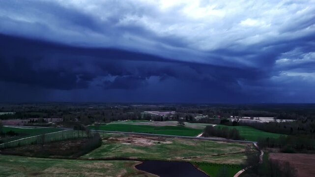 Aerial panorama capturing massive dark shelf cloud storm front rolling over flat green farmlands on outskirts of Jelgava, Latvia