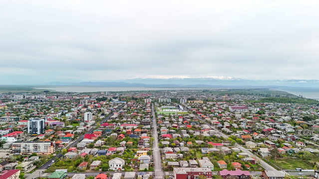 Coastal town on the black sea with residential houses and buildings lining a long road. Featuring distant snow capped mountains and an overcast sky