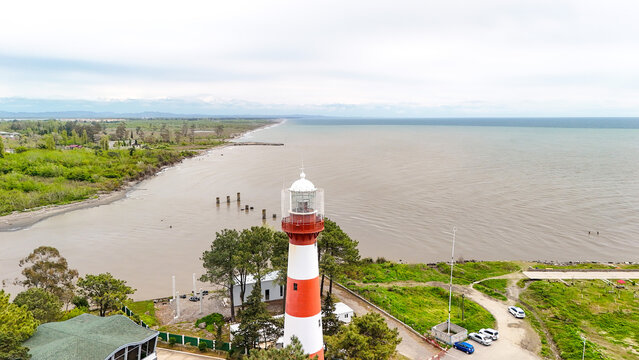 Red and white striped lighthouse standing tall on the poti coastline, offering scenic views of the vast black sea, a green natural landscape, and the distant horizon