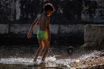 Fototapeta premium Boy playing barefoot in shimmering water splashes
