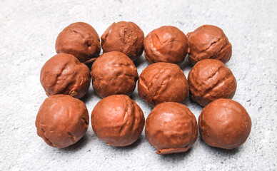 Obraz premium Close up of many chocolate candy balls with broken peanut filling on gray background, top view. Pile of chocolate balls in a bowl.