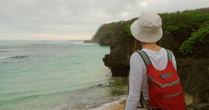 Backpacker woman looking at scenic tropical coastline with crystal clear ocean in Bali