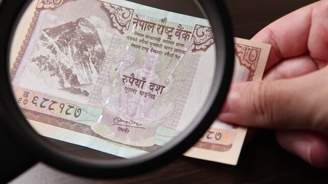 Examination of 10 Nepalese rupee (NPR) cash money with magnfication glass, loupe. Concept of authenticity check, fight against counterfeiting of banknotes, anti fraud measures in Nepal. Close up view.
