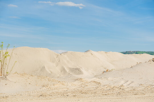 View of large sand piles and dunes at an industrial quarry under a bright blue sky in Futog, Vojvodina, Serbia.