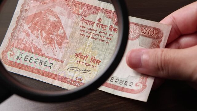 Examination of 20 Nepalese rupee (NPR) cash money with magnfication glass, loupe. Concept of authenticity check, fight against counterfeiting of banknotes, anti fraud measures in Nepal. Close up view.