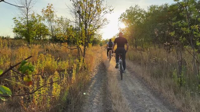 Young male friends ride mountain ski bikes along trail on sunny summer day. Beautiful golden sunlight at background. Concept of active lifestyle, adventure spirit and carefree weekend outdoor
