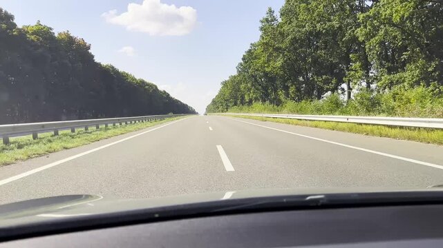 POV from moving car at sunny summer day. Through the windshield white lane marking runs steadily along asphalt road, creating a clear sense of speed, rhythm and open daytime travel