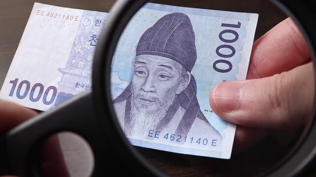 Examination of 1000 South Korean Won (KRW) cash money with magnfication glass, loupe. Concept of authenticity check, fight against counterfeiting of banknotes, anti fraud measures in South Korea.