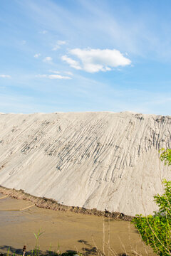 View of a large white sand pile with erosion grooves under a clear blue sky with a single cloud in Futog, Vojvodina, Serbia.