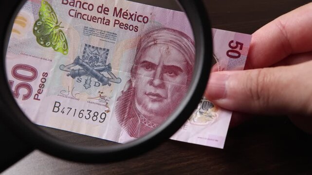 Examination of 50 Mexican Peso (MXN) cash money with magnfication glass, loupe. Concept of authenticity check, fight against counterfeiting of banknotes, anti fraud measures in Mexico. Close up view.