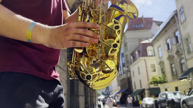Male fingers of musician play the saxophone on summer day. Natural light reflects off metal surface, highlighting movement and rhythm. Scene captures live urban music and atmosphere street performance