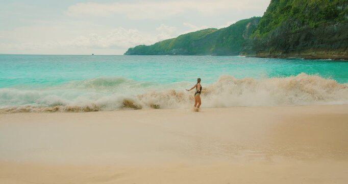 Cheerful woman playing in white ocean surf on tropical sandy beach in Bali Nusa Penida