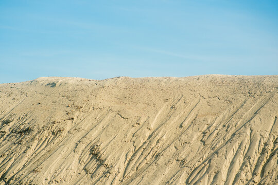 View of a large sand dune with textured erosion patterns under a clear blue sky in Futog, Vojvodina, Serbia.