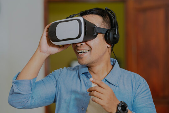 Asian man looking at vr box, virtual reality glasses at home. People and technology metaverse concept, viewing 360 videos.
