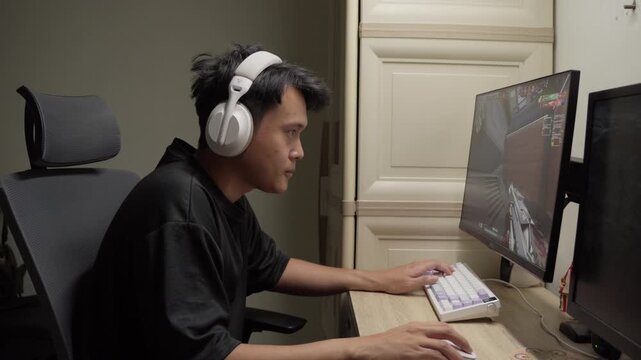 Side View of Intense Asian Gamer Clench Fist in Celebration During Valorant FPS Match on PC