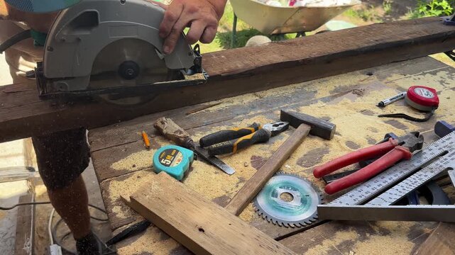 Arms of professional repairman sawing wooden construction with a circular saw at construction. Male hands of adult craftsman cuts wood using electric grind wheel at the site. Slow motion