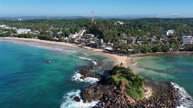Aerial view of the turquoise ocean water surrounding Parrot Rock and the sandy coast. Mirissa, Sri Lanka