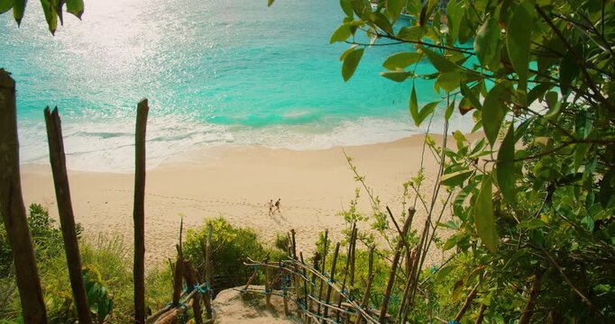 People walking on white sand of Kelingking beach near turquoise water in Nusa Penida Bali