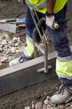 Construction worker positioning concrete curbstone with metal lifter The Concept of precision and manual labor