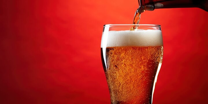Pouring golden beer with frothy head into a clear glass on a red background