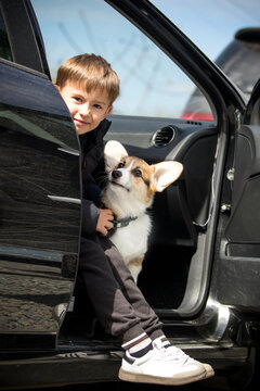 Smiling boy and Corgi puppy sitting together in a car door.