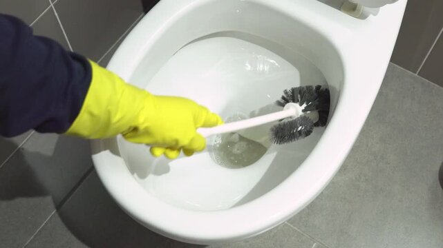 Scrubbing and cleaning. Shot of a woman hand with yellow glove cleaning a bathroom toilet.