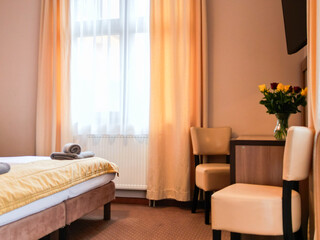 Kolorowy bukiet czerwonych i żółtych róż ustawiony na stoliku w jasnym pokoju hotelowym. Przytulne wnętrze z łóżkami w tle podkreśla komfortowy i gościnny charakter miejsca noclegowego. © Freshfanpage
