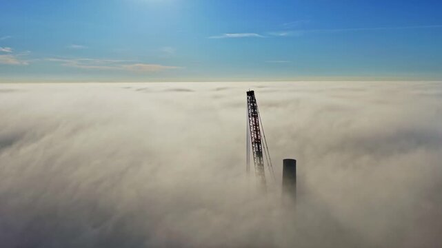Crane tower rising through a thick blanket of fog