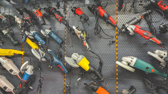 A large selection of electric angle grinders and power tools hanging on a black pegboard wall in a professional hardware store. Various industrial grinders for metal and stone processing on displa
