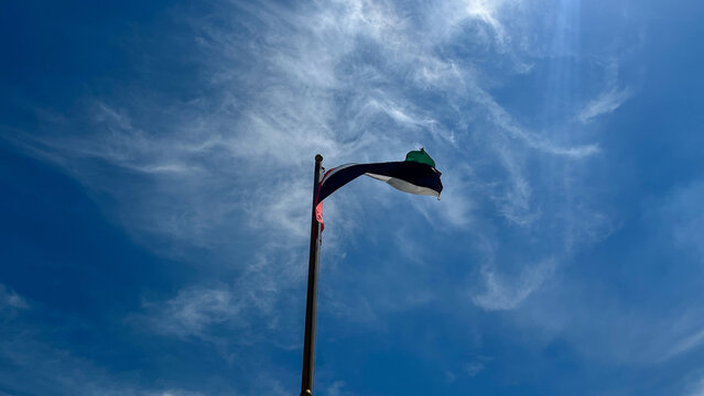Low angle view of the United Arab Emirates flag waving on a flagpole against a clear blue sky with soft wispy clouds