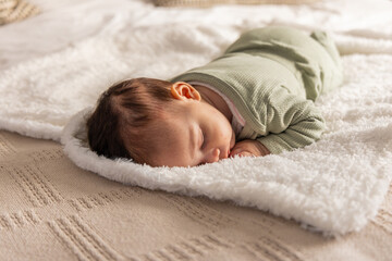 Female infant sleeping on stomach at home on white fleece blanket wearing pale green onesie © wavebreak3