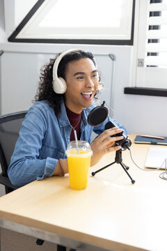 Non-binary host speaking into mic by window, wearing denim jacket and headphones