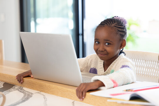 African American child sitting at bar in kitchen studying on silver laptop with colored pencils