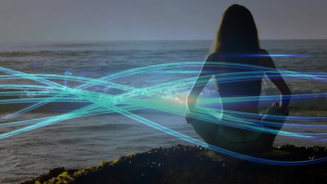 Woman sitting rock ledge facing ocean, ribbons sweeping, causing arms extending toward glow, tech