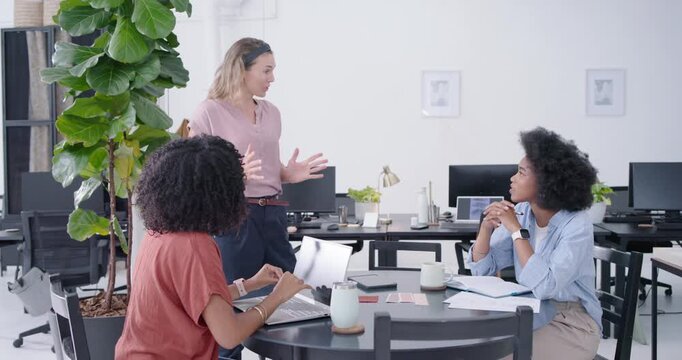 Diverse women at round table in office, lead coming, arranging pink cards for project with laptop
