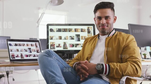 Man sitting in digital office reacting to camera cue, smiling as monitors showing thumbnails