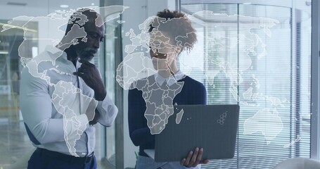 Reviewing colleagues wearing white shirt and dark sweater sharing laptop in glass office, world map © vectorfusionart