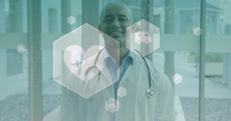 Naklejka premium Standing physician in white lab coat, blue shirt, with stethoscope, showing hexagon icons in clinic