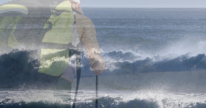 Paddling woman wearing fluorescent yellow life jacket cutting through ocean surf, paddle and spray