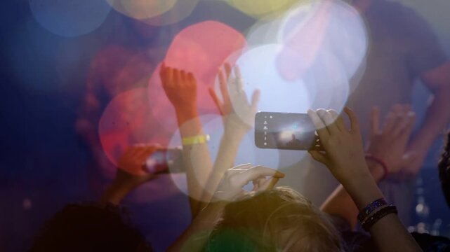 Vertical video: Raising center fan holding phone filming stage at concert with wristband and bokeh
