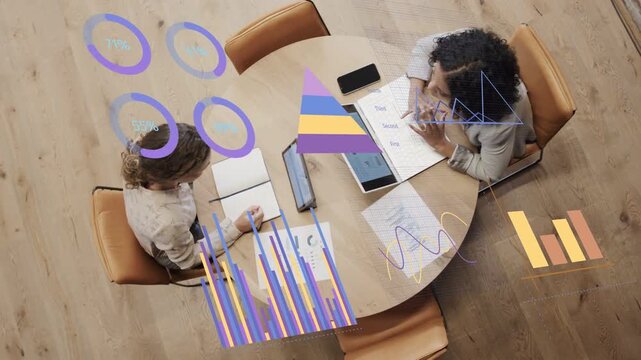 Right woman tapping tablet and showing data on table while left scribe noting driving business goal