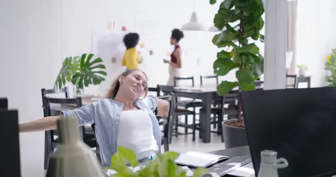 Woman in striped top leaning stretching checking watch writing in notebook at desk resuming work