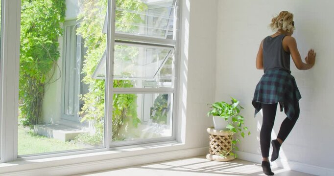African American woman starting one-foot, balancing and stretching calf by window, copy space