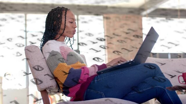 Woman typing on laptop in loft starting tech work with binary overlay, pausing, adjusting posture